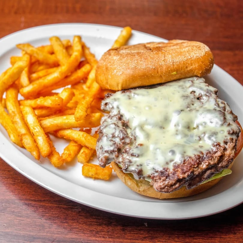 A cheesy burger with a side of golden french fries on a white plate.
