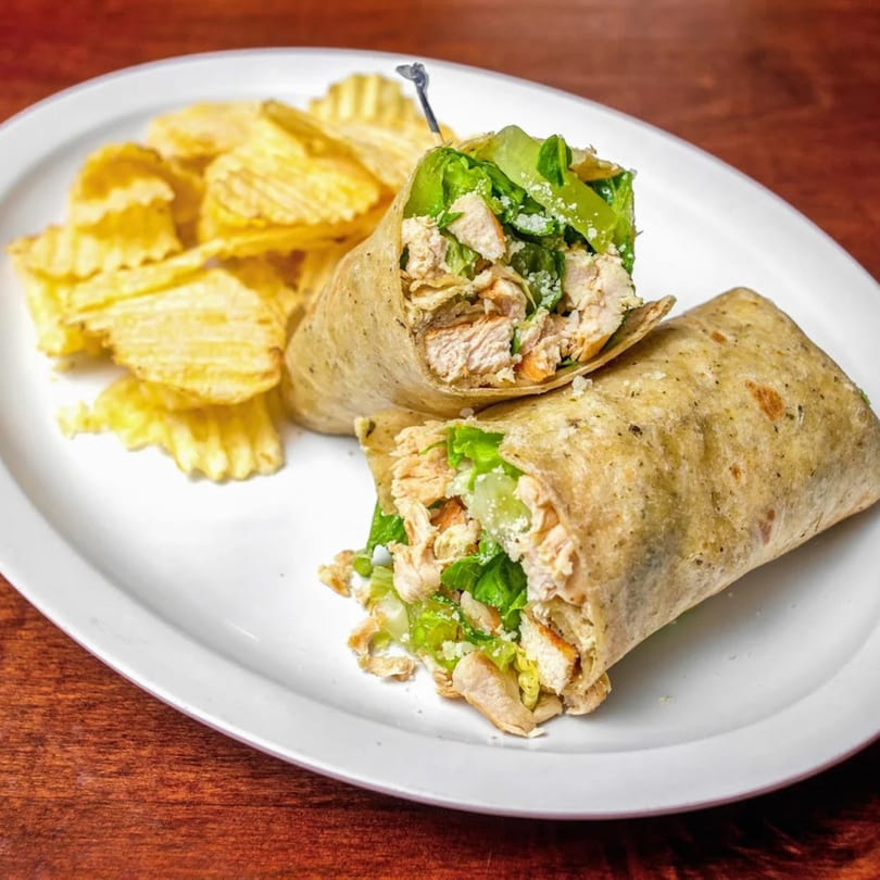 Two chicken Caesar wraps with lettuce and cheese, served with a side of ridged potato chips.