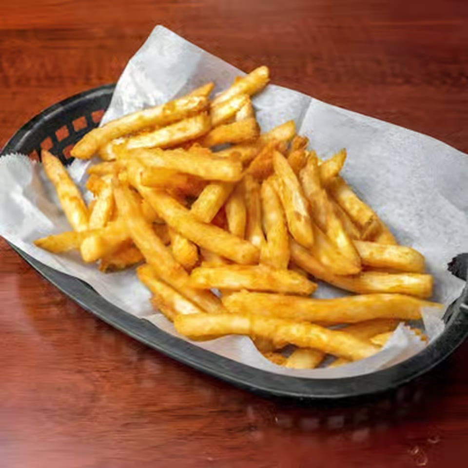A black basket filled with golden-brown French fries, lined with white paper, on a wooden table.