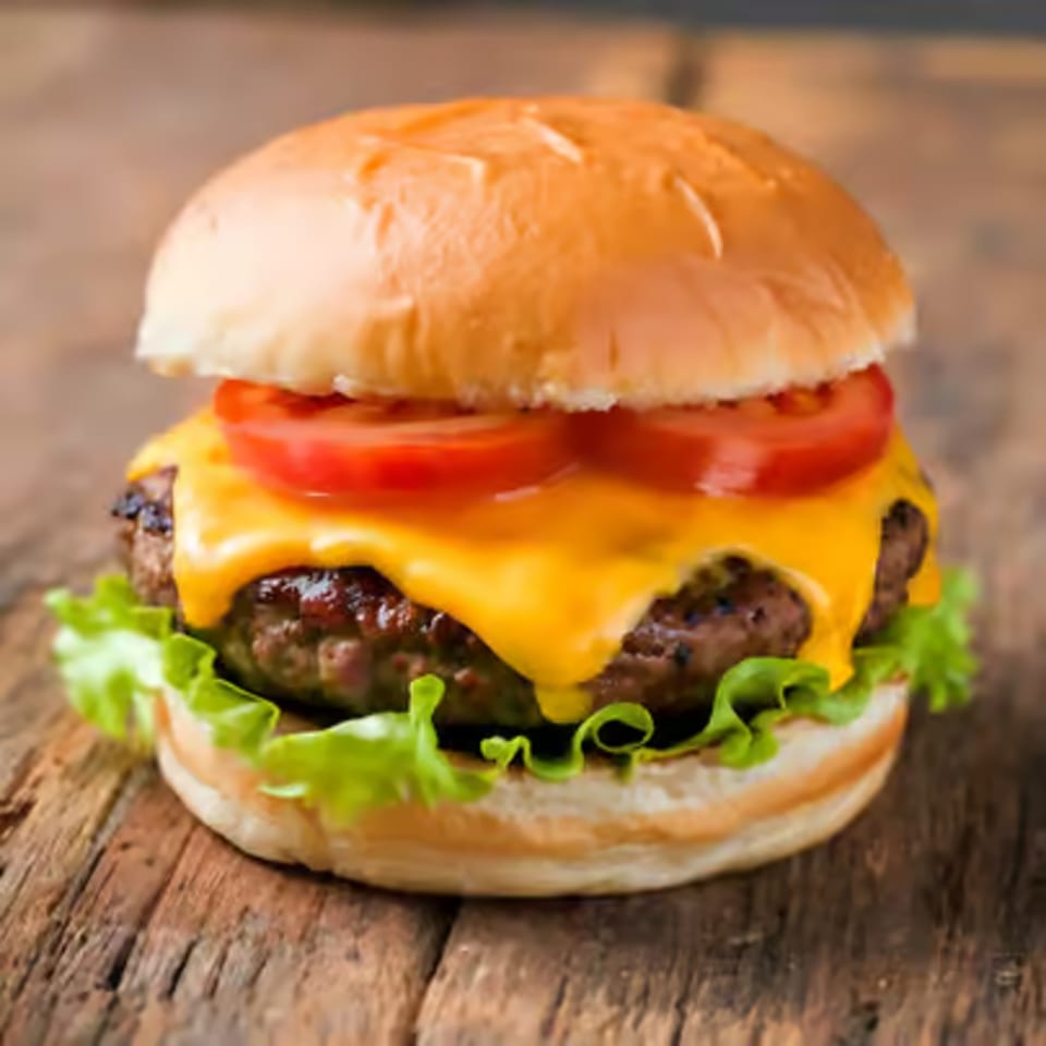 Cheeseburger with melted cheese, tomatoes, and lettuce on a wooden surface.